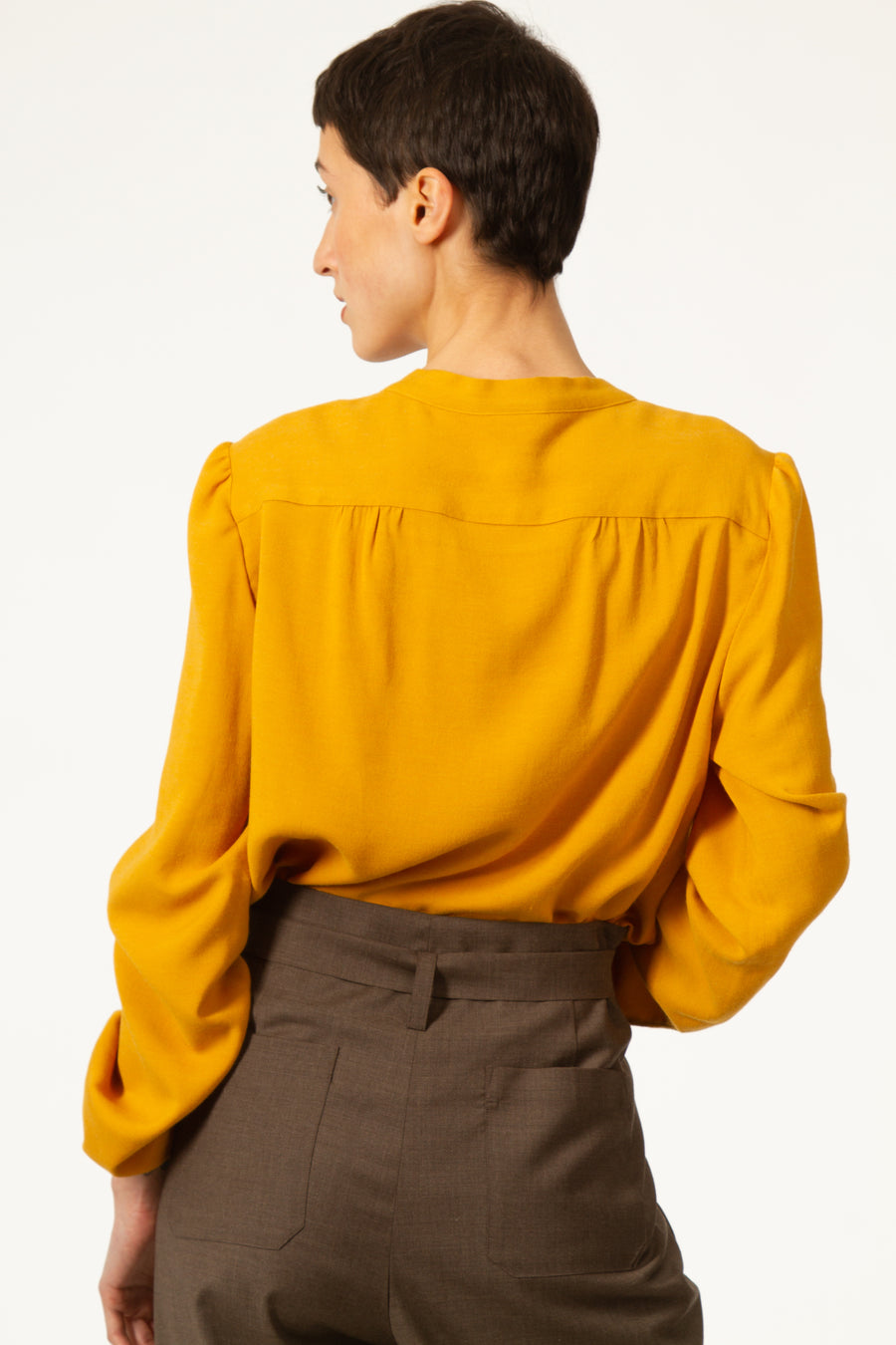 Top JEAN Jaune à col rond et noué sur le côté. Blouse asymétrique en voile viscose laine. Empiècement sur le dos et les épaules. Manches longues avec poignets boutonnés.